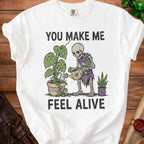 Skeleton watering plants with text "You Make Me Feel Alive".