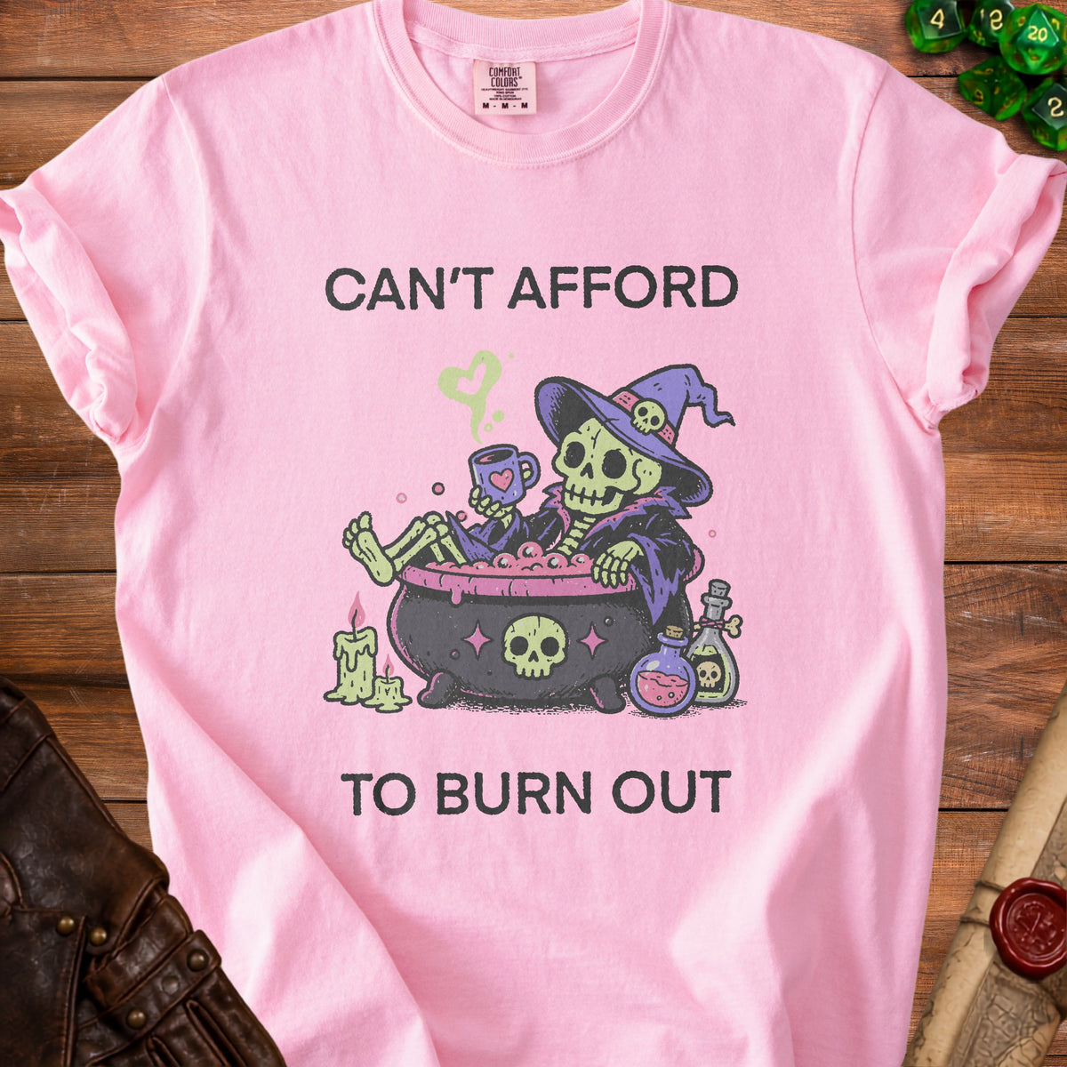 Pink t-shirt with skeleton witch illustration and text "CAN'T AFFORD TO BURN OUT".
