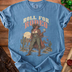 Blue t-shirt with graphic of a cowgirl demon holding a D20 die and text "Roll for Rodeo".