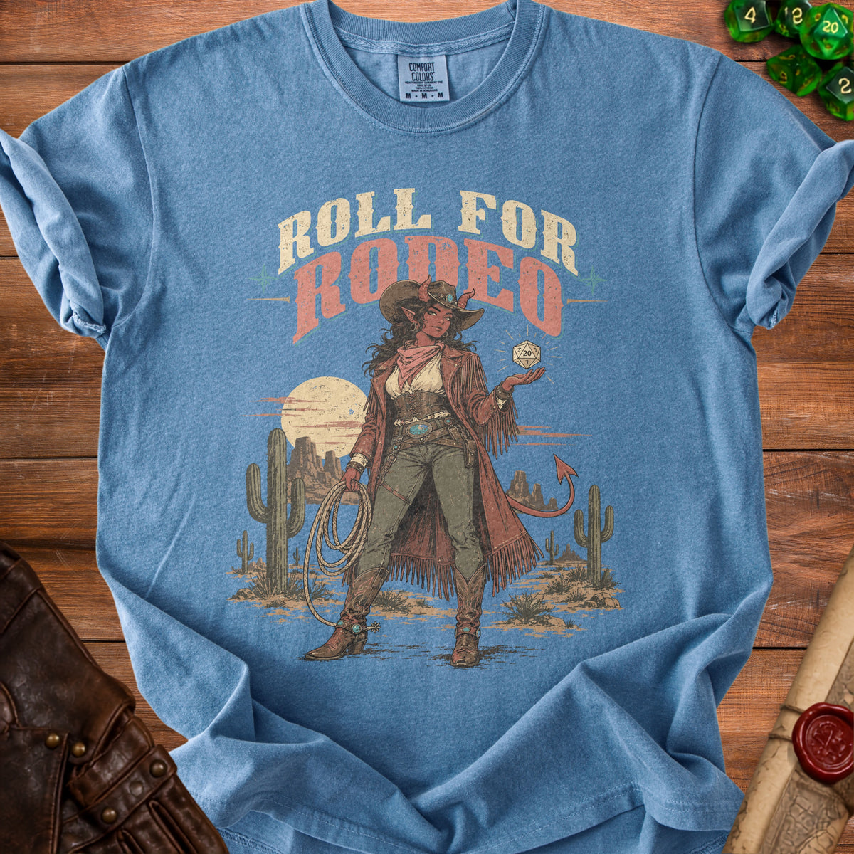 Blue t-shirt with graphic of a cowgirl demon holding a D20 die and text "Roll for Rodeo".
