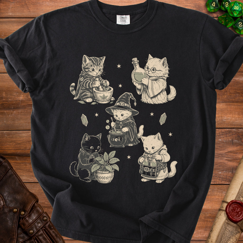 Black t-shirt featuring five vintage-style illustrations of cats practicing witchcraft, surrounded by stars and crystals.