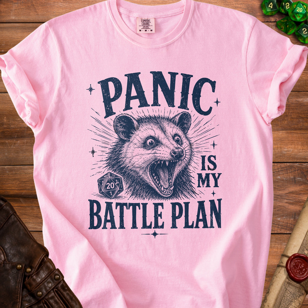 Pink t-shirt with dark blue text and graphic of a panic-stricken opossum and dice.