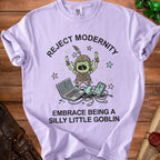 Lilac t-shirt with a goblin illustration and text reading "REJECT MODERNITY EMBRACE BEING A SILLY LITTLE GOBLIN."
