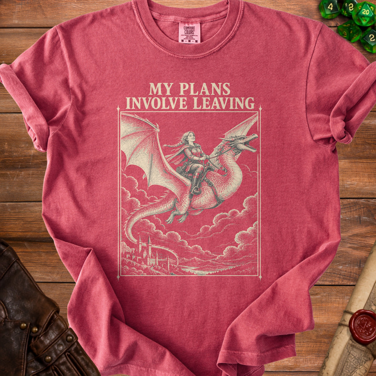 A red t-shirt with a vintage-style graphic of a woman riding a dragon above clouds, bearing the text MY PLANS INVOLVE LEAVING.