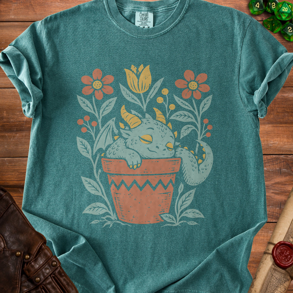 Teal t-shirt with a sleeping dragon in a potted plant surrounded by flowers.