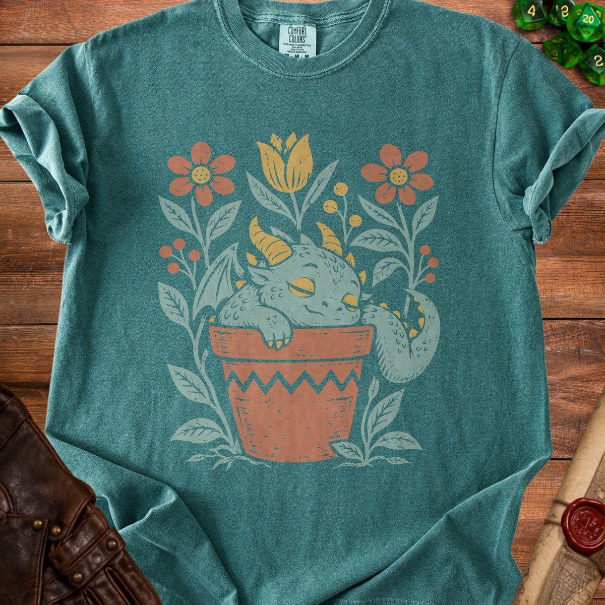 Teal t-shirt with a sleeping dragon in a potted plant surrounded by flowers.
