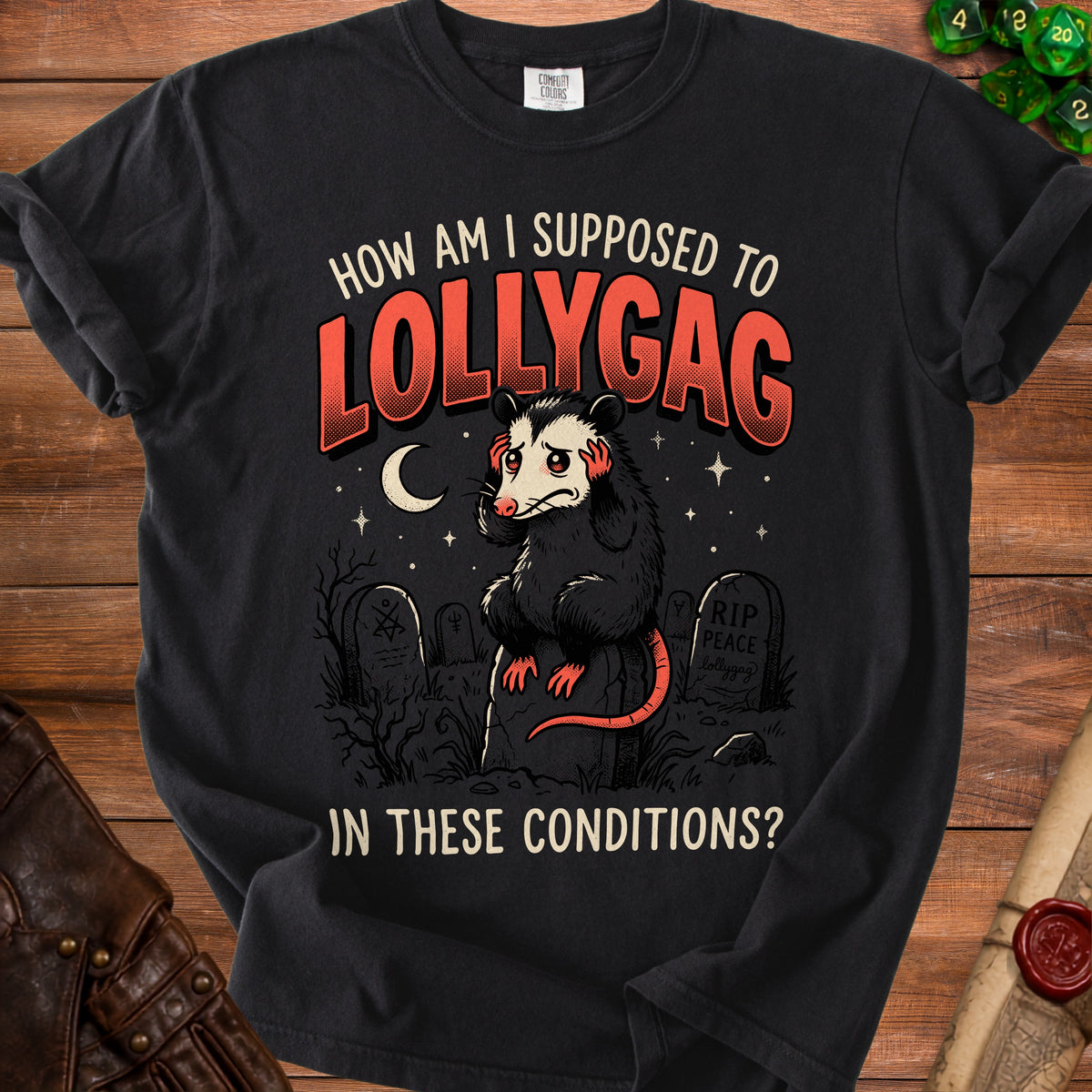 Black t-shirt graphic featuring an opossum in a graveyard with text "HOW AM I SUPPOSED TO LOLLYGAG IN THESE CONDITIONS?".