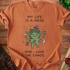 Orange t-shirt with cartoon goblin and text "MY LIFE IS A MESS AND I LOVE THE CHAOS".