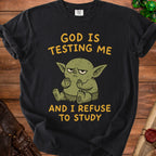 Black t-shirt with cartoon green creature and text "God is Testing Me and I Refuse to Study".