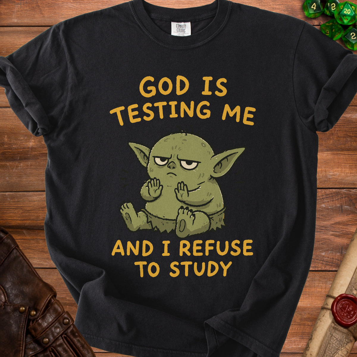 Black t-shirt with cartoon green creature and text "God is Testing Me and I Refuse to Study".
