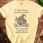 Yellow t-shirt with an illustration of a gnome house and the text "I don't know what lies ahead... but I do know it will be an adventure."
