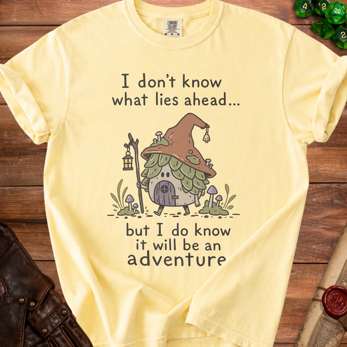 Yellow t-shirt with an illustration of a gnome house and the text "I don't know what lies ahead... but I do know it will be an adventure."