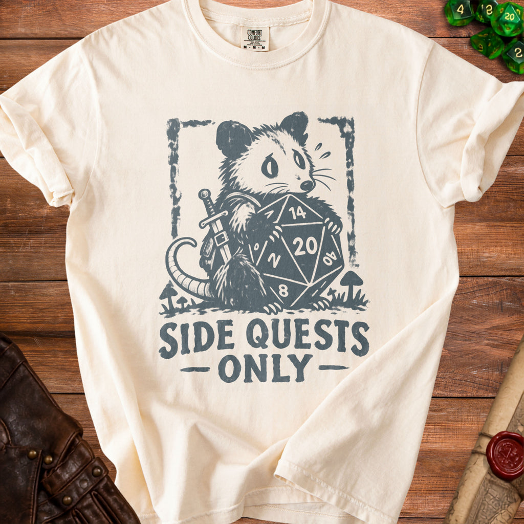 Cream t-shirt with opossum graphic holding a D20 die and sword, text "Side Quests Only".