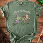Green t-shirt with illustration of wizard and knight, text "ABRA CA STABRA".