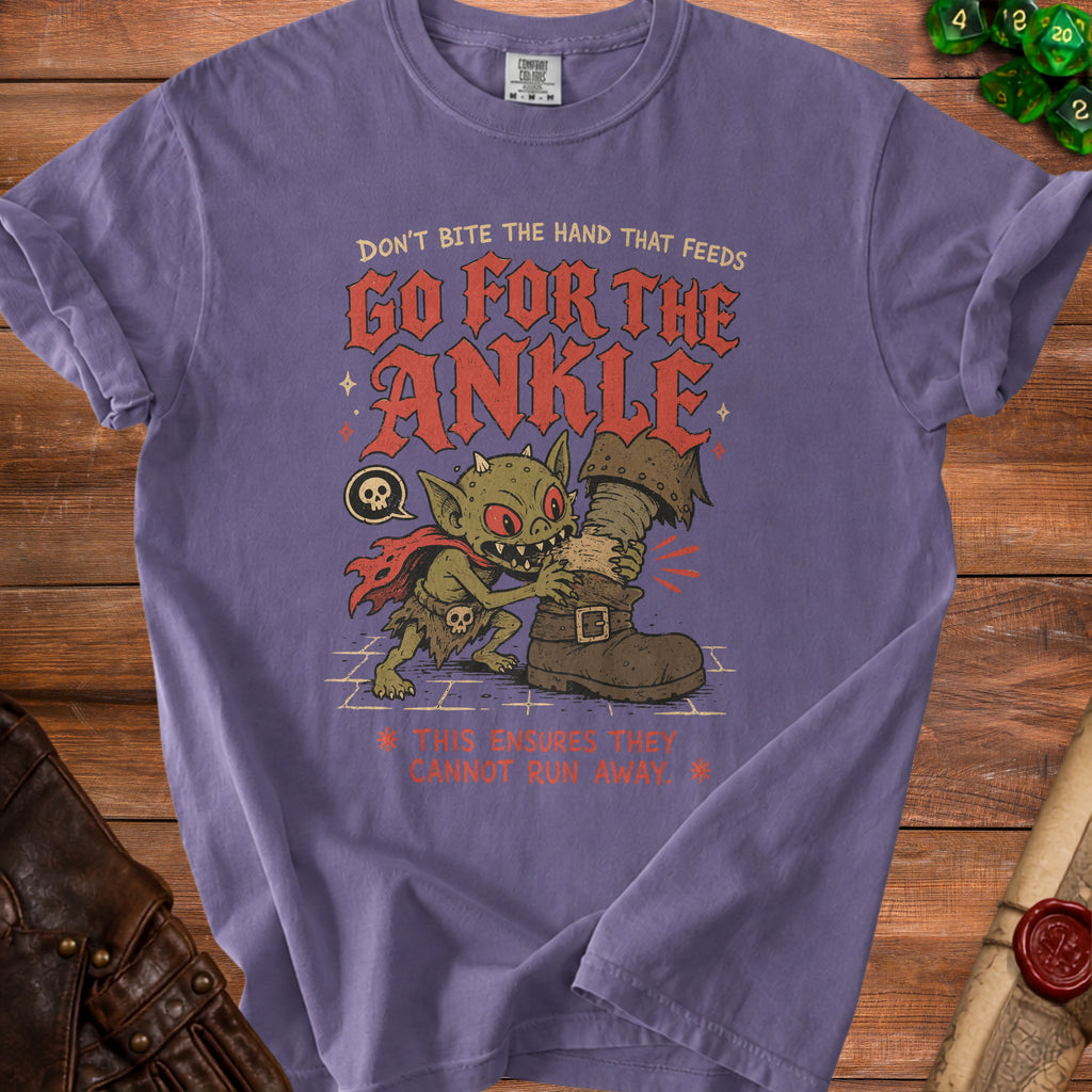 Purple t-shirt with goblin biting a boot and text "GO FOR THE ANKLE".