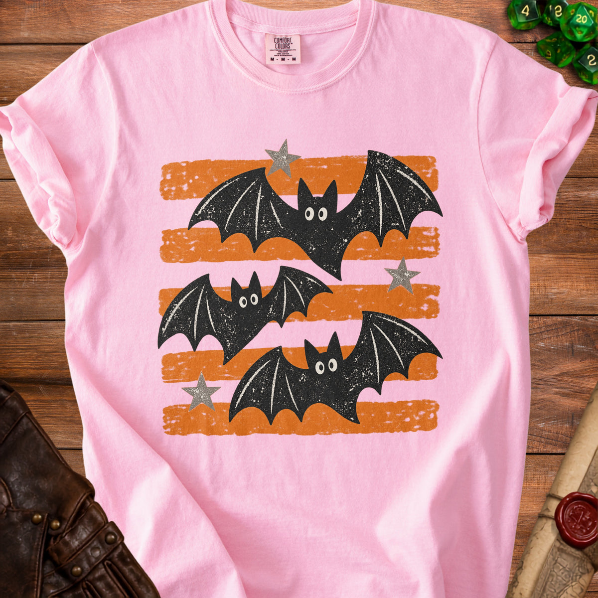 Pink t-shirt with distressed graphic of black bats and grey stars on orange stripes.