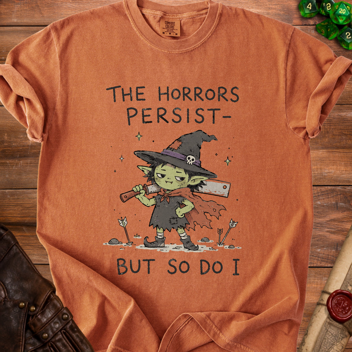 Orange t-shirt with a goblin wearing a witch hat and holding cleavers, text reads "The Horrors Persist - But So Do I".