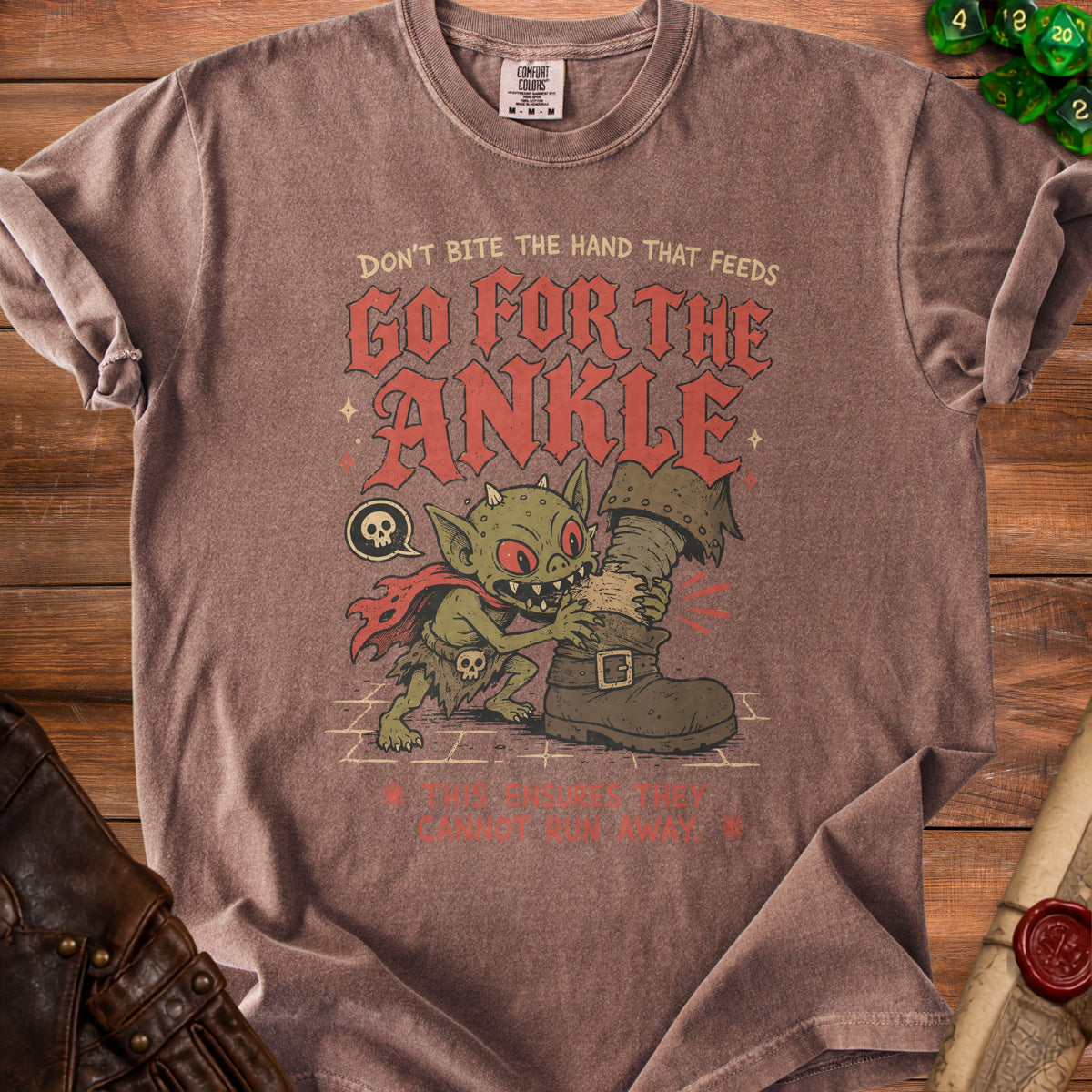 Brown t-shirt with a goblin biting a boot and text "Don't bite the hand that feeds, go for the ankle."