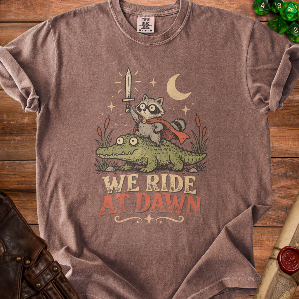 T-shirt with raccoon holding sword riding alligator, text "WE RIDE AT DAWN".