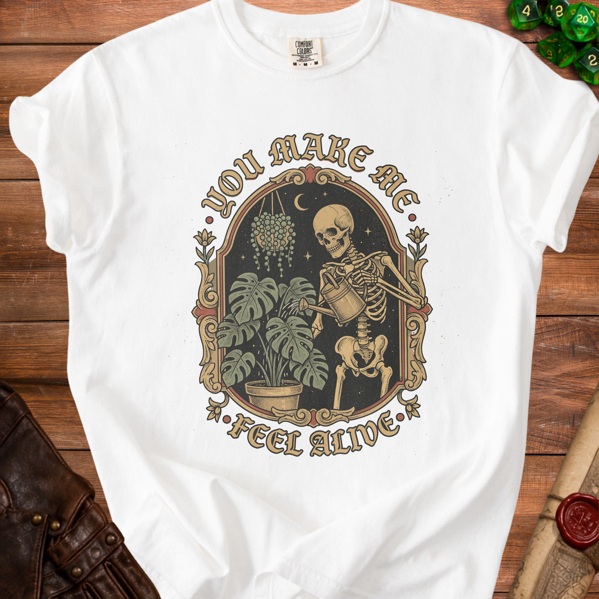 White t-shirt with skeleton watering plants and text "You Make Me Feel Alive".