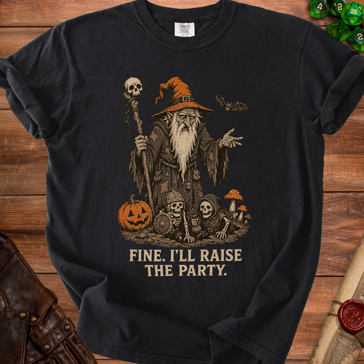 Dark t-shirt with wizard, skeletons, pumpkin, and bat illustration; text reads "FINE. I'LL RAISE THE PARTY."