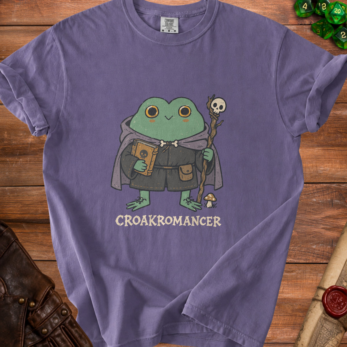 Frog wizard holding a book and staff, with "CROAKROMANCER" text on a purple t-shirt.