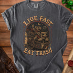 T-shirt with "Live Fast Eat Trash" text and artwork of creatures in a cart.