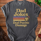 Dark gray t-shirt with text "Dad Jokes Deal Psychic Damage" and a d20 die.