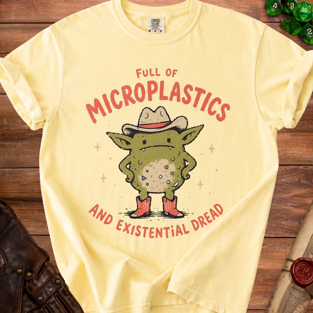Yellow t-shirt with graphic of a goblin in a cowboy hat and boots, reading "Full of Microplastics and Existential Dread".