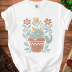White t-shirt with a distressed print of a sleeping dragon in a terracotta pot with flowers.