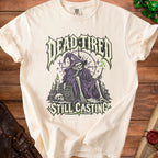 Cream t-shirt with "DEAD TIRED STILL CASTING" graphic featuring a skeleton wizard.