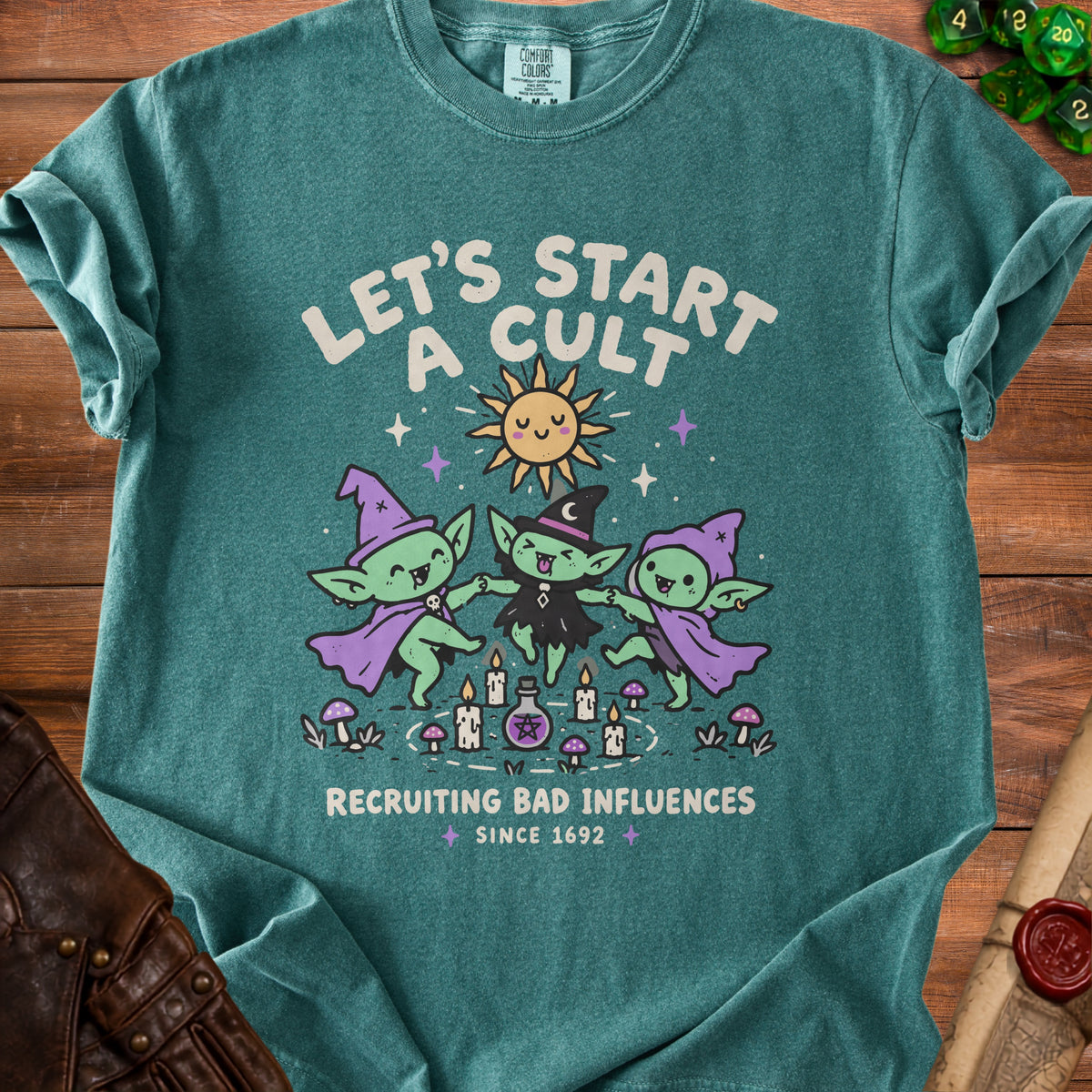 Teal shirt with graphic of three goblins dancing around candles, sun, and potion. Text reads "Let's Start a Cult Recruiting Bad Influences Since 1692".