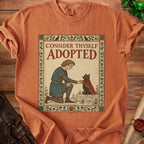Orange t-shirt with "CONSIDER THYSELF ADOPTED" text and medieval knight petting a cat.