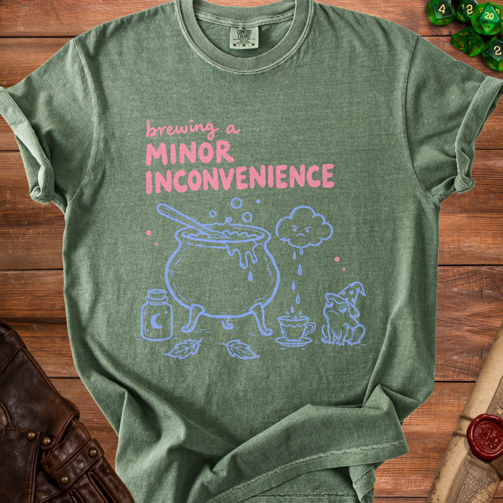 Green t-shirt with "brewing a minor inconvenience" text and cauldron graphic.