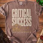 Brown t-shirt with "Critical Success" text, a twenty-sided die, and dice.