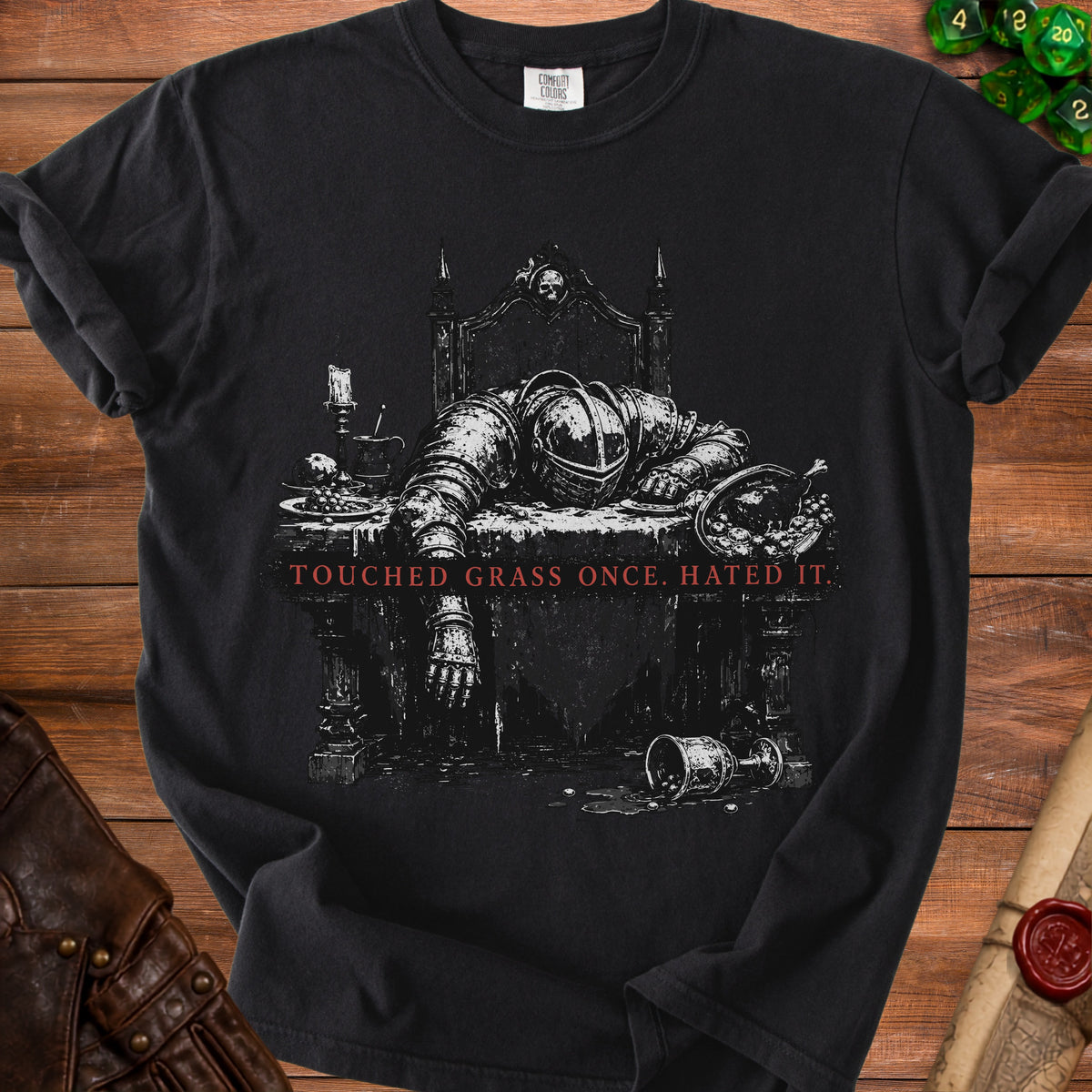 Black t-shirt graphic of knight in armor slumped over table with text "TOUCHED GRASS ONCE. HATED IT."