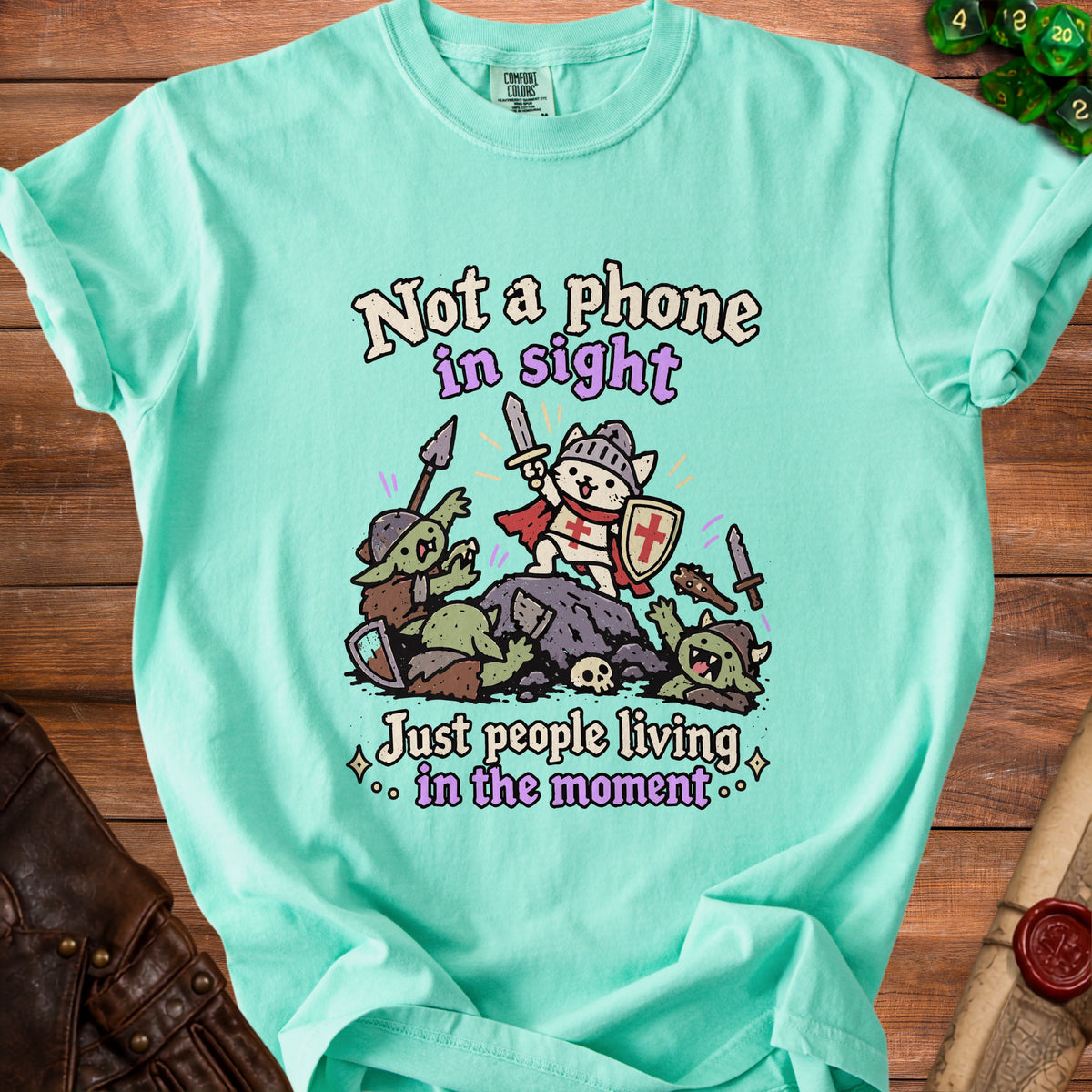Aqua t-shirt with cartoon cat knight battling goblins and text "Not a phone in sight. Just people living in the moment."