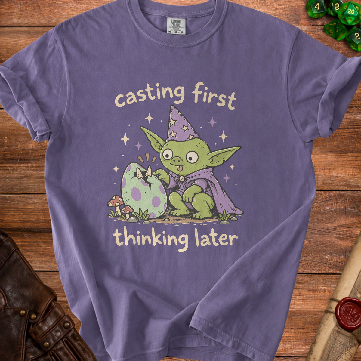 Purple t-shirt with green goblin wizard hatching a dragon egg, text "casting first thinking later".