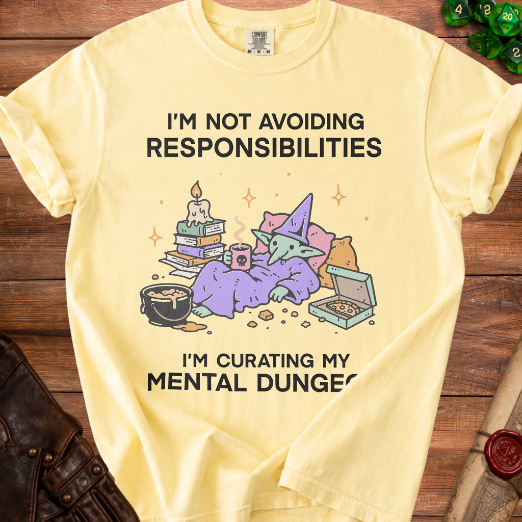 Yellow t-shirt with text "I'M NOT AVOIDING RESPONSIBILITIES I'M CURATING MY MENTAL DUNGE" and cartoon goblin.