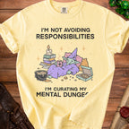 Yellow t-shirt with text "I'M NOT AVOIDING RESPONSIBILITIES I'M CURATING MY MENTAL DUNGE" and cartoon goblin.