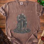 Brown t-shirt with "still here" and a knight kneeling with a sword.