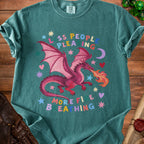 Teal t-shirt with pink dragon breathing fire, stars, hearts, and the words "Less People Pleasing More Fire Breathing".