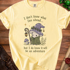 Light yellow t-shirt with a graphic of a mushroom adventurer and the text "I don't know what lies ahead... but I do know it will be an adventure".