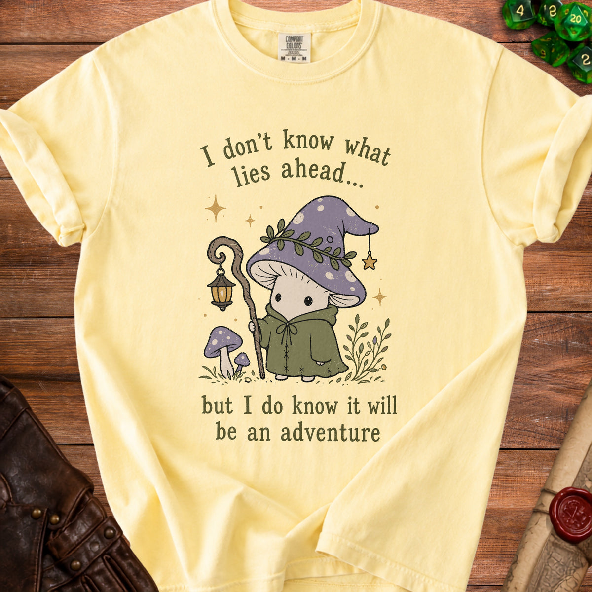 Light yellow t-shirt with a graphic of a mushroom adventurer and the text "I don't know what lies ahead... but I do know it will be an adventure".