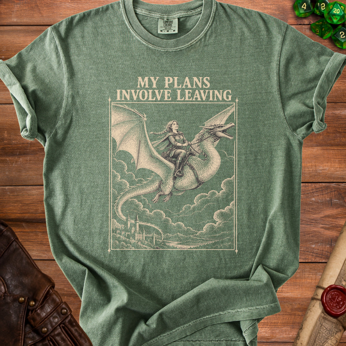 Muted green t-shirt featuring the text MY PLANS INVOLVE LEAVING above an illustration of a woman riding a dragon.