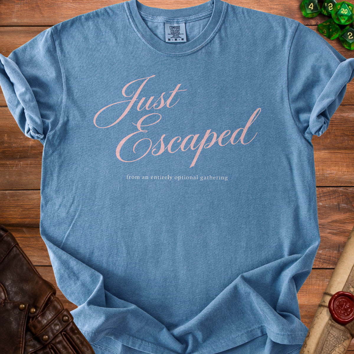A blue t-shirt with pink cursive text reading Just Escaped from an entirely optional gathering.