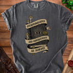 Dark gray t-shirt with a graphic of a book with an eye, mushrooms, and banners reading "Overstimulated and Underleveled as Always".