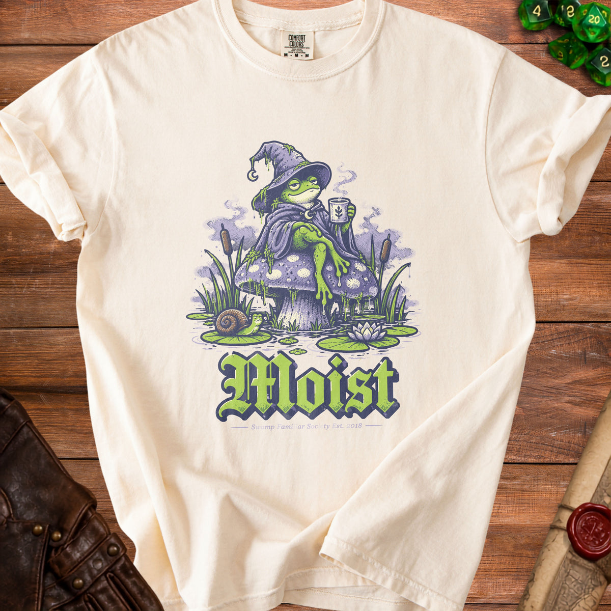 Cream t-shirt with graphic of frog wizard, mushroom, and text "Moist".
