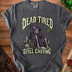 Dark t-shirt with skeleton wizard graphic and text "DEAD TIRED STILL CASTING".