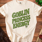 Cream t-shirt with green text "GOBLIN PRINCESS ENERGY" and a mushroom icon.